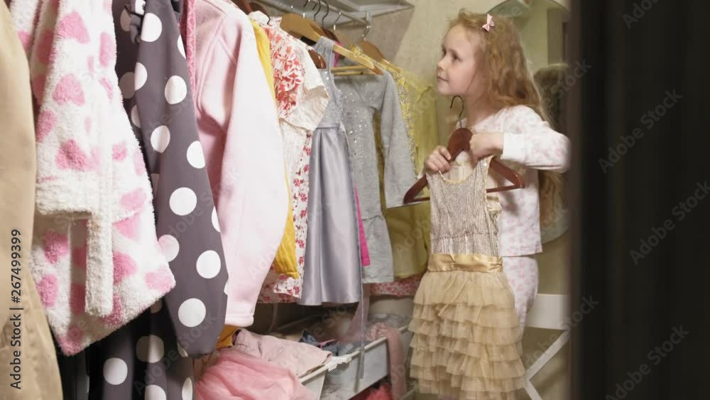 Beautiful little girl chooses dress in home wardrobe. Beauty and fashion Beautiful little girl chooses dress in home wardrobe. Beauty and fashion