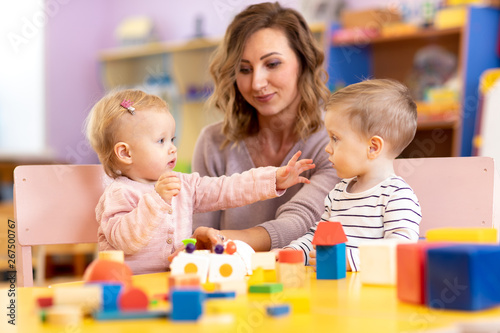 Babies with mentor in kindergarten. Kids toddlers in nursery school. Little girl and boy preschoolers playing with teacher.