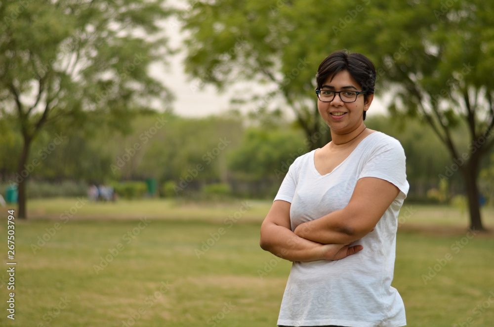 Smart Indian woman standing, posing for the camera with hands crossed in a park wearing white in summers in Delhi, India