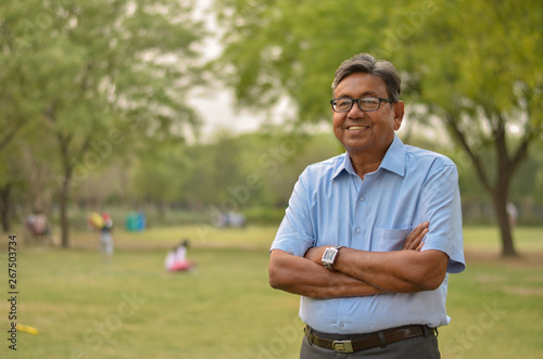 Portrait of a happy senior Indian man wearing a suit in the outside setting standing and thinking with hands crossed in a park in Delhi, India