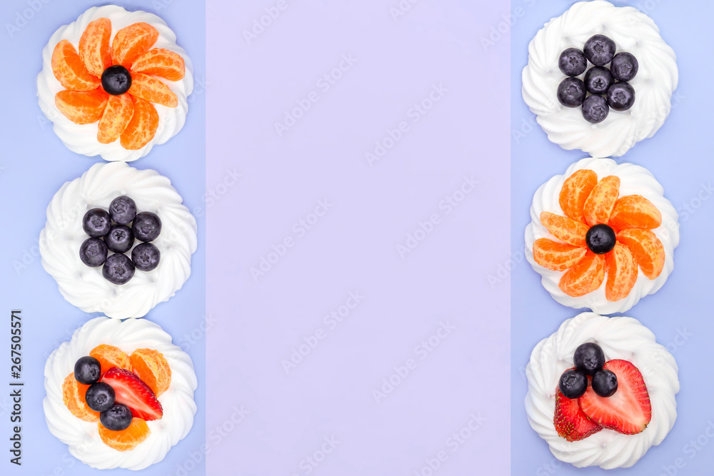 Fototapeta premium Frame of meringue with blueberries, strawberries and tangerines on a lavender background. Top view