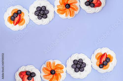 Fototapeta Naklejka Na Ścianę i Meble -  Frame of meringue with blueberries, strawberries and tangerines on a lavender background. Top view