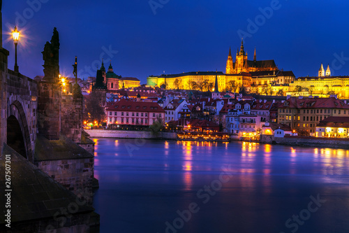 Looking along the Charles Bridge toward the illuminated St. Vitus Cathedral and Prague Castle at twilight