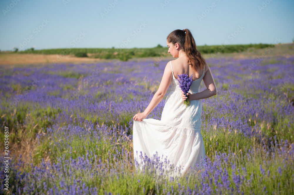 adult pretty woman in white summer dress holding lavender bouquet behind her back standing in blooming meadow concept of beauty in nature adult pretty woman in white summer dress holding lavender bouquet behind her back standing in blooming meadow concept of beauty in nature