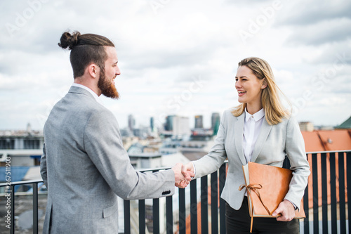 Two young business people standing on a terrace outside office, shaking hands. photo