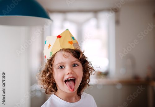 A small girl with a paper crown at home, having fun when looking at camera. photo