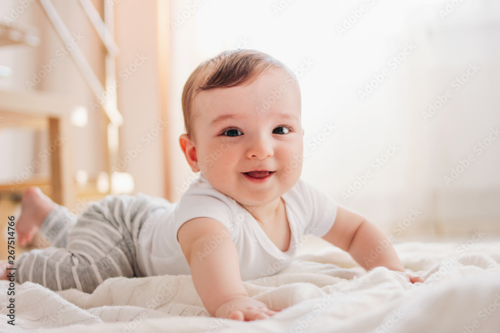 Charming little baby boy 6 months looking at the camera on white blanket in home Charming little baby boy 6 months looking at the camera on white blanket in home