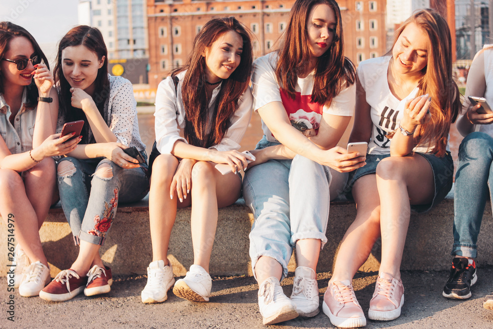 Obraz premium Group of young happy girls real friends students using mobile at city street on sunset background