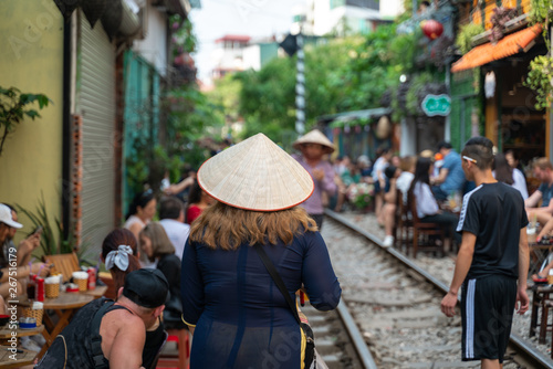 Foreign tourist with Vietnamese conical hat walking on railroad in Hanoi. People drink coffee or walking on railways waiting for train to arrive on railway road on background in Hanoi, Vietnam.