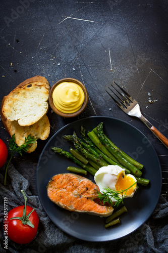 Salmon fish steak grilled with asparagus, poached egg on black background. Healthy food. Top view flat lay. Free space for your text.