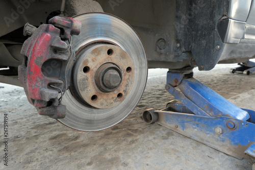 Old dirty car hoisted on a jack. Close-up of a wheel arch without a wheel. Tire installation or repair of the brake system of the car. © romsvetnik