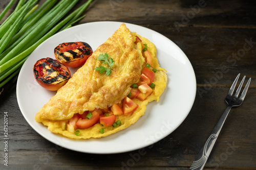 omelette tomato sliced and grill on white dish decorated with spring onion. wood table light side.