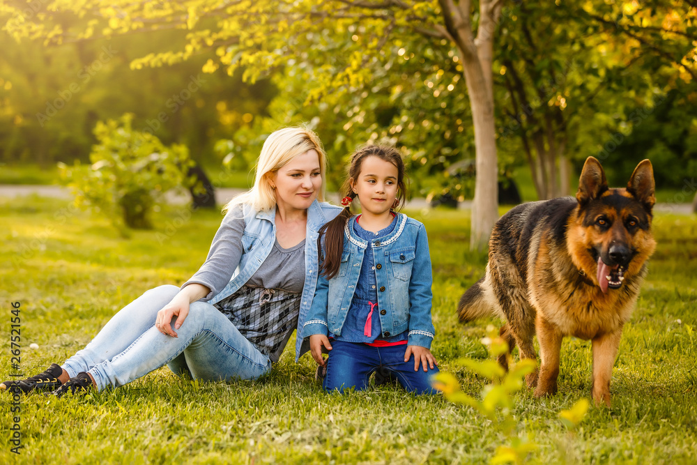 Fototapeta premium Mother and daughter with pet sitting on the grass at the summer park
