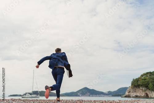Businessman running to the sea holding in hand briefcase. Back view