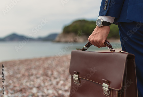 Businessman holding in hand briefcase on background the beach 