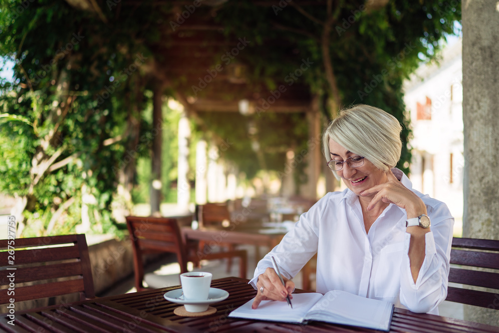 Happy senior woman writing to notebook or diary at a cafe Happy senior woman writing to notebook or diary at a cafe