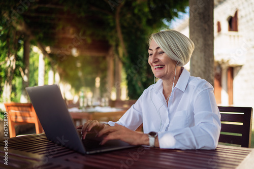 Happy mature woman having a video chat through laptop computer while resting at the cafe photo