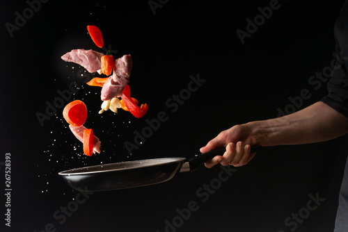 chef prepares meat with vegetables, on a black background, roasting, tasty food, recipe book, menu, restaurant business