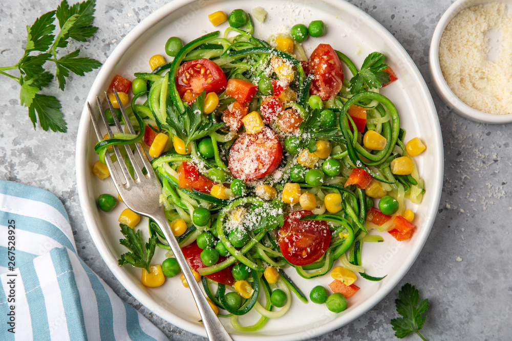 zucchini noodle with tomato, corn and green peas on white plate