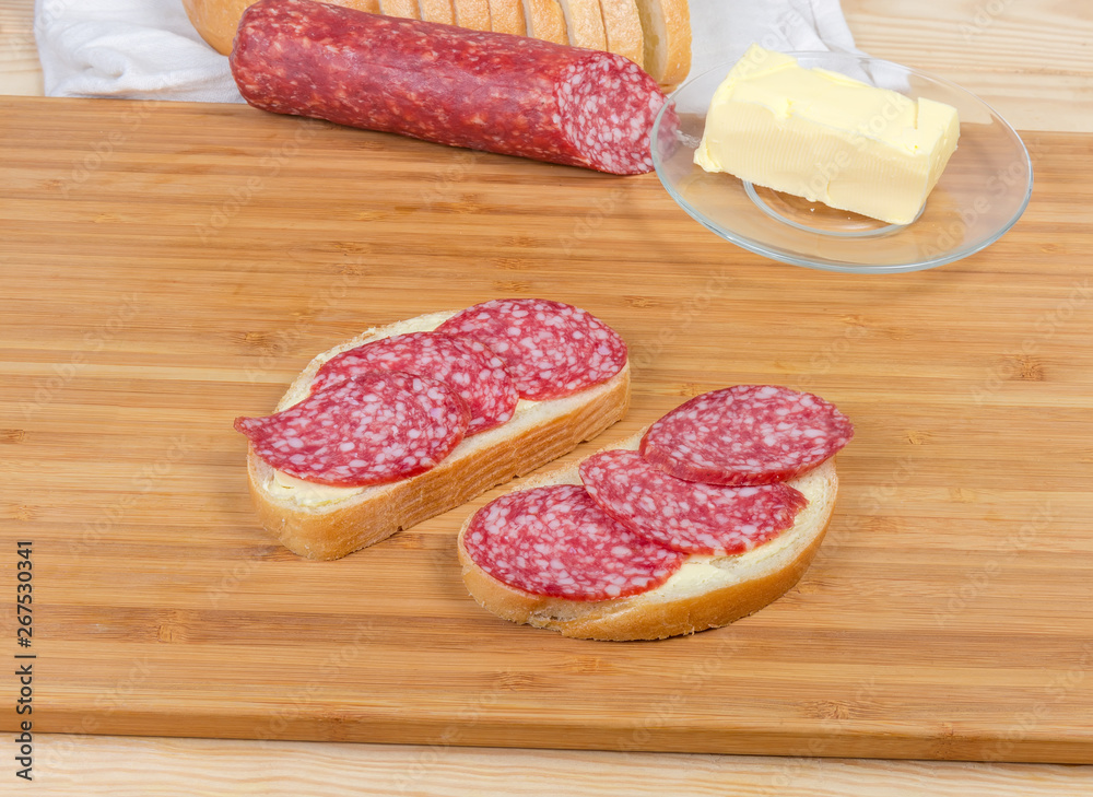 Open sandwiches with salami on bamboo cutting board agains ingredients Open sandwiches with salami on bamboo cutting board agains ingredients