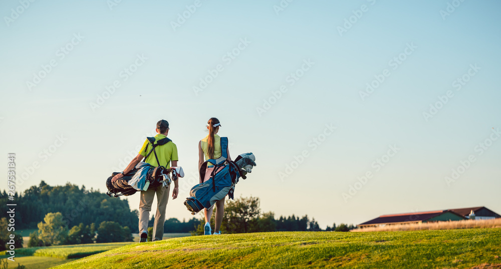 Happy couple carrying stand bags towards the golf course in a sunny day Happy couple carrying stand bags towards the golf course in a sunny day
