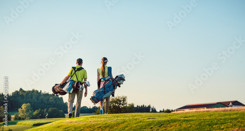Happy couple carrying stand bags towards the golf course in a sunny day