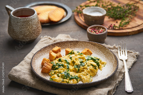 Scrambled eggs with spinach, cup of tea on dark brown background. Breakfast with Pan-fried omelette, side view, close up
