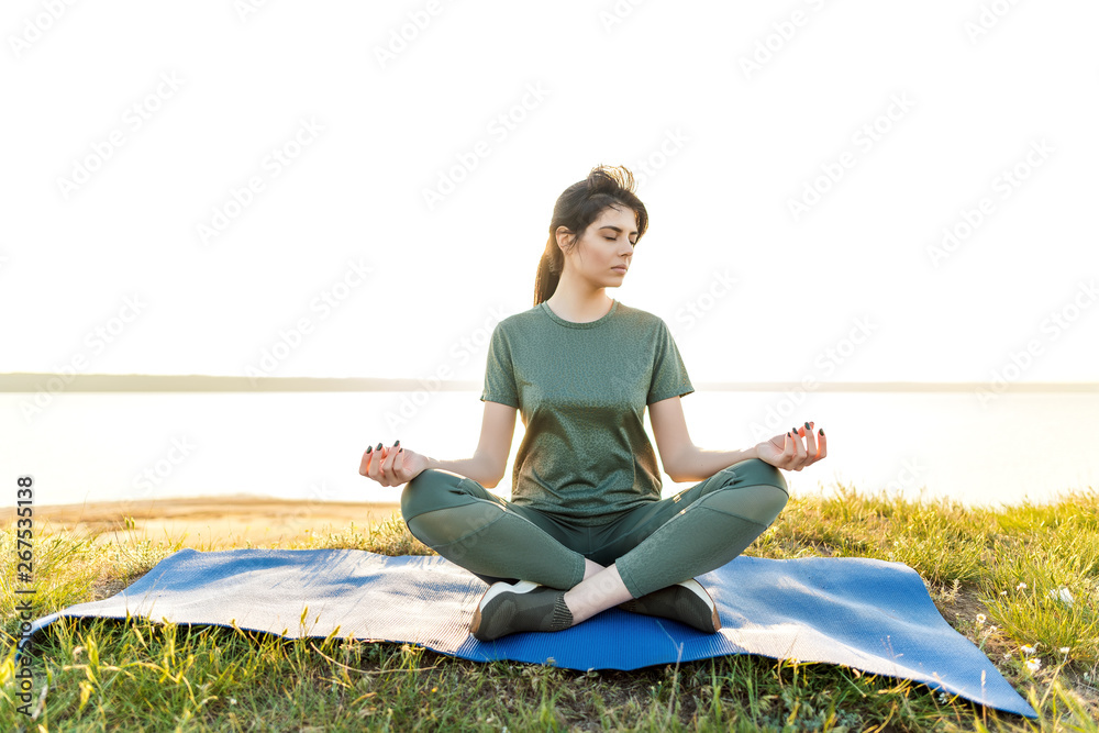 Attractive woman doing yoga on the sunset near the sea with a beach on a hill. Lifestyle picture of beautiful girl meditating, smiling and exercising on the nature Attractive woman doing yoga on the sunset near the sea with a beach on a hill. Lifestyle picture of beautiful girl meditating, smiling and exercising on the nature