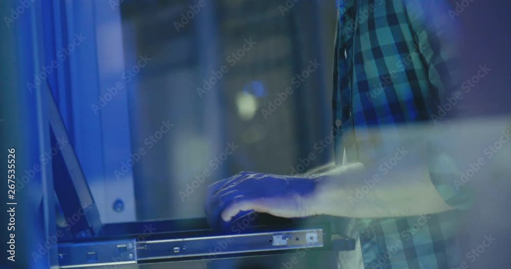 Male server engineer in glasses works with laptop in large data center