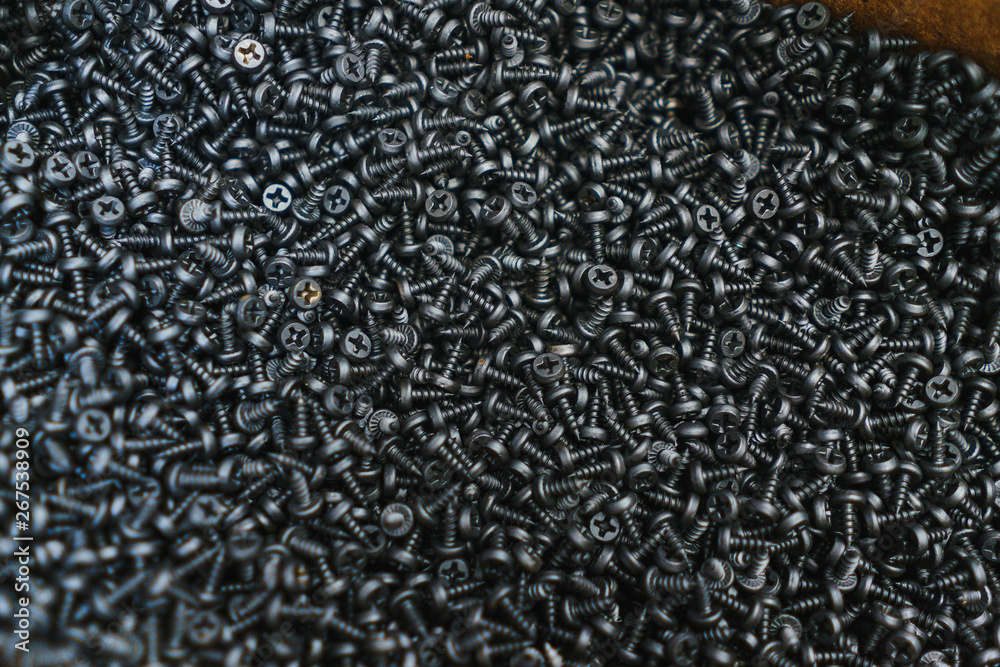 Many black small screws for repair and fasteners in a box close-up. Many black small screws for repair and fasteners in a box close-up.