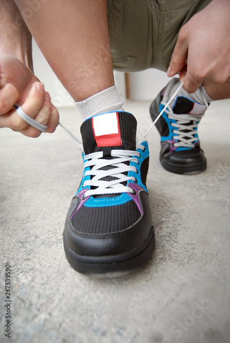 A man in shorts and sneakers goes on a marble tile. Close-ups of sneakers on the background of a gray wall. The athlete tied the laces.