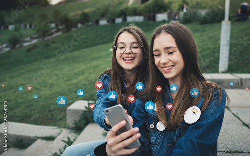 Two happy young best friends using social media on their smartphon in city park