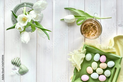 Springtime flat lay in pastel colors, white tulips, cup of green tea and sugar Easter eggs on light wood photo