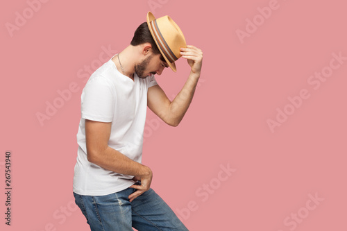 Photography Profile side view portrait of bearded young dancer man in white shirt holding his hat and standing in michael jackson dancing pose