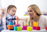 Nursery baby and mother or teacher play with montessori toys at table in daycare centre