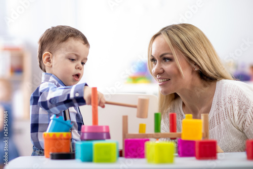 Nursery baby and mother or teacher play with montessori toys at table in daycare centre