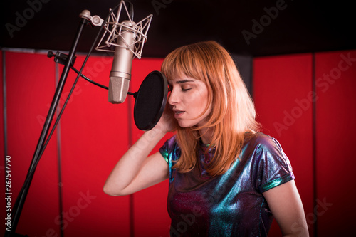 Female singer with microphone recording a song in music studio © leszekglasner