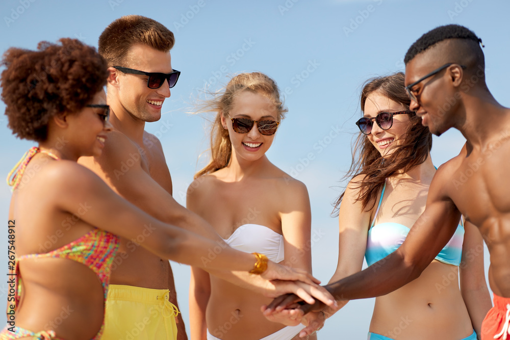 friendship, summer holidays and people concept - group of happy friends stacking hands together on beach