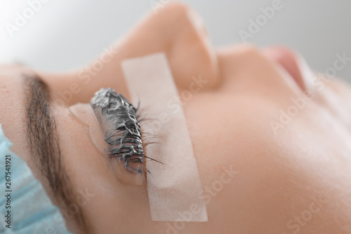 Young woman undergoing procedure of eyelashes dyeing and lamination in beauty salon, closeup