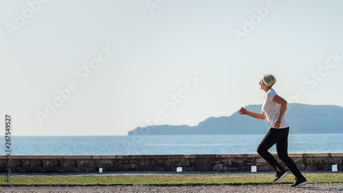 Senior woman jogging at sunrise. Morning running on background the sea and mountains