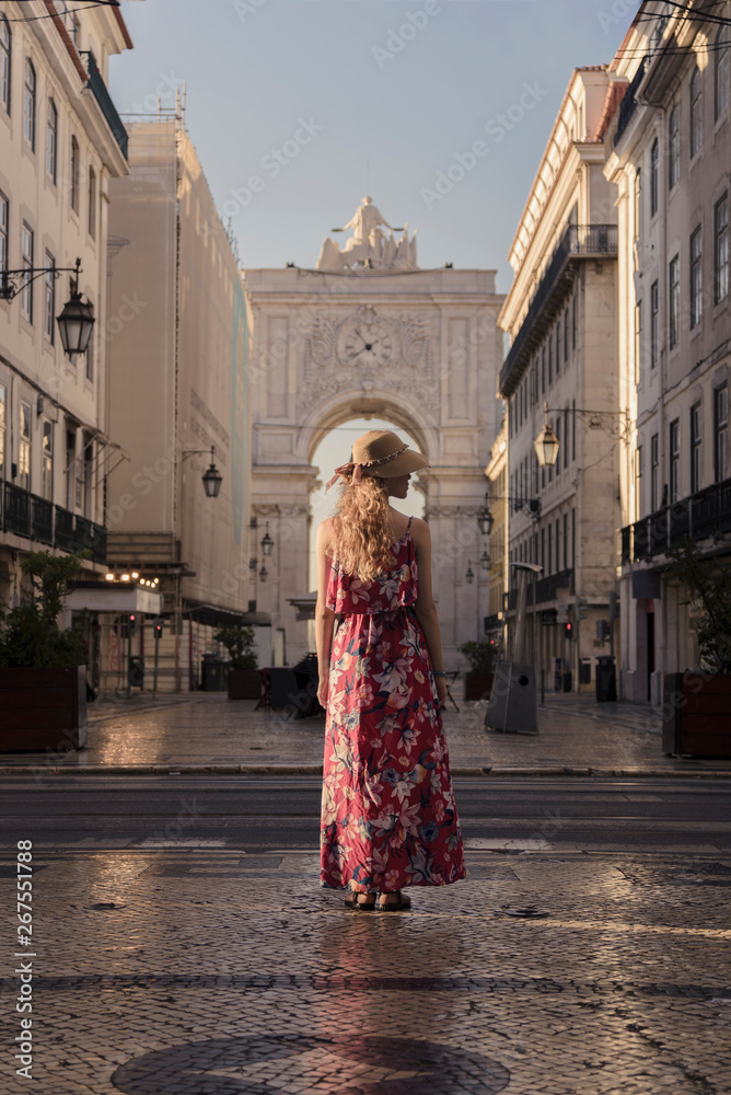 Naklejka premium Young blonde tourist woman walking on the Rua Augusta street in Lisbon city and exploring old architecture, Portugal