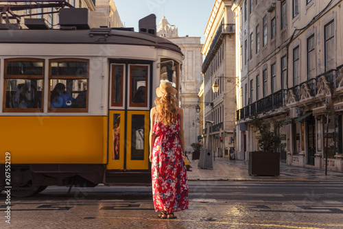 Young blonde tourist woman looking at passing typical Lisbon yellow tram on the street in the city centre on Rua Augusta