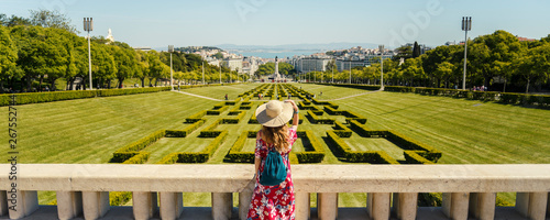 Young blonde woman wearing red generic sundress and a hat looking at cityscape view of Lisbon, capital city of Portugal