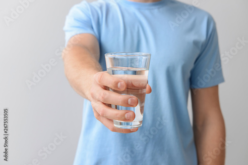 Man with glass of fresh water on light background, closeup