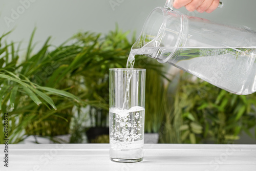Pouring of fresh water into glass on table photo