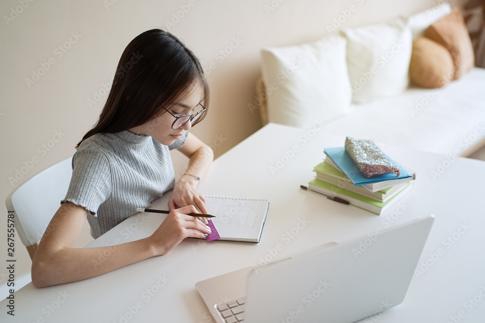 Cute teenager girl sitting at table with books and doing homework. Education, children and school concept Cute teenager girl sitting at table with books and doing homework. Education, children and school concept