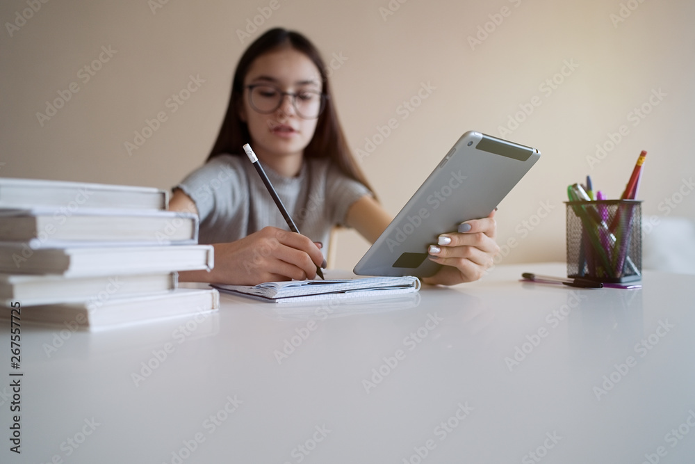 Cute teenager girl sitting at table with books and doing homework. Education, children and school concept Cute teenager girl sitting at table with books and doing homework. Education, children and school concept
