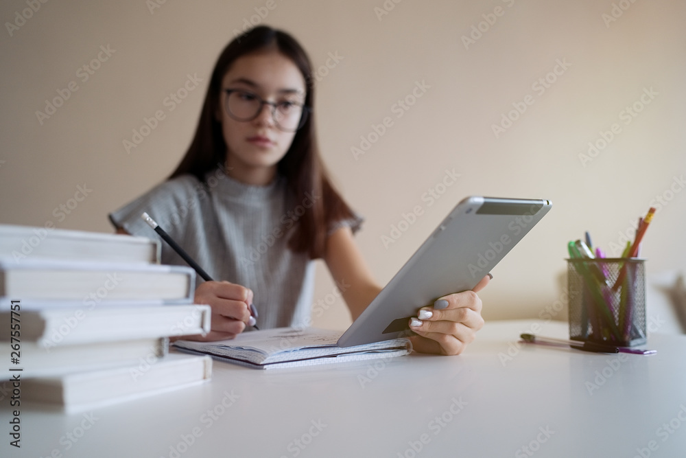 Cute teenager girl sitting at table with books and doing homework. Education, children and school concept Cute teenager girl sitting at table with books and doing homework. Education, children and school concept