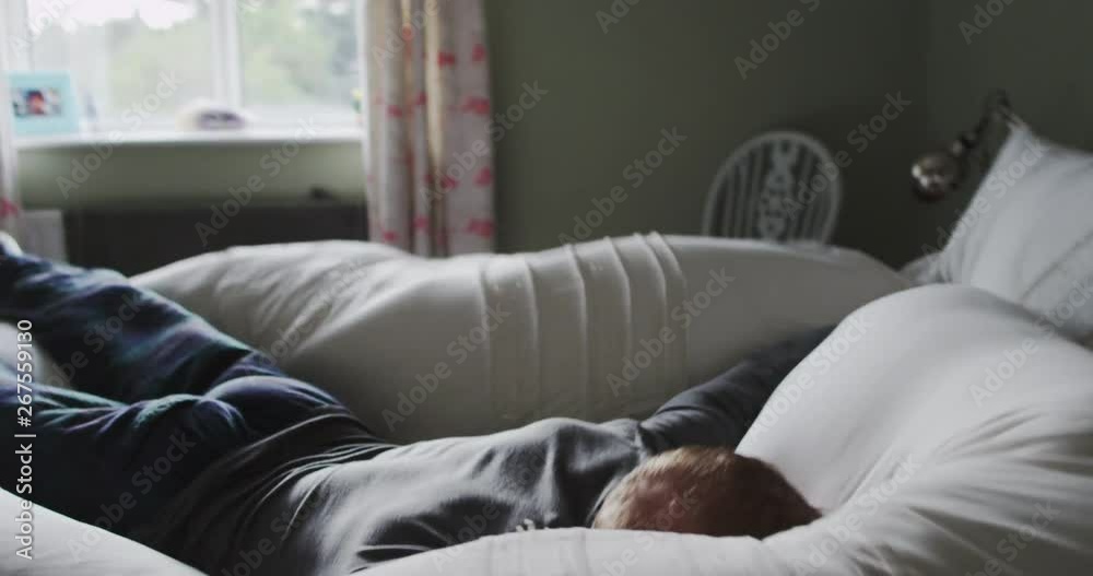 4K Ecstatic man jumping face-first & lying spreadeagled onto soft comfy bed. Slow motion.
