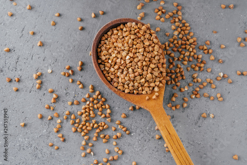 Uncooked brown buckwheat in wooden spoon against grey background. Organic food concept. Buckwheat grains. Ingredients for cooking porridge photo